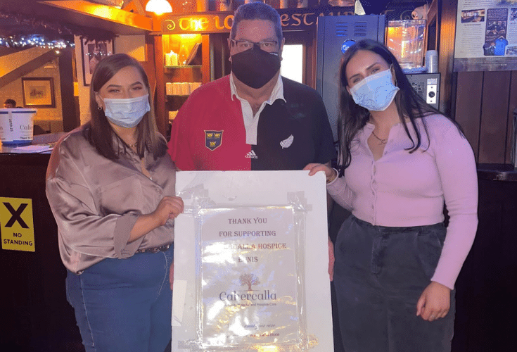 Lecturer and two female students holding poster for charity at a pub quiz